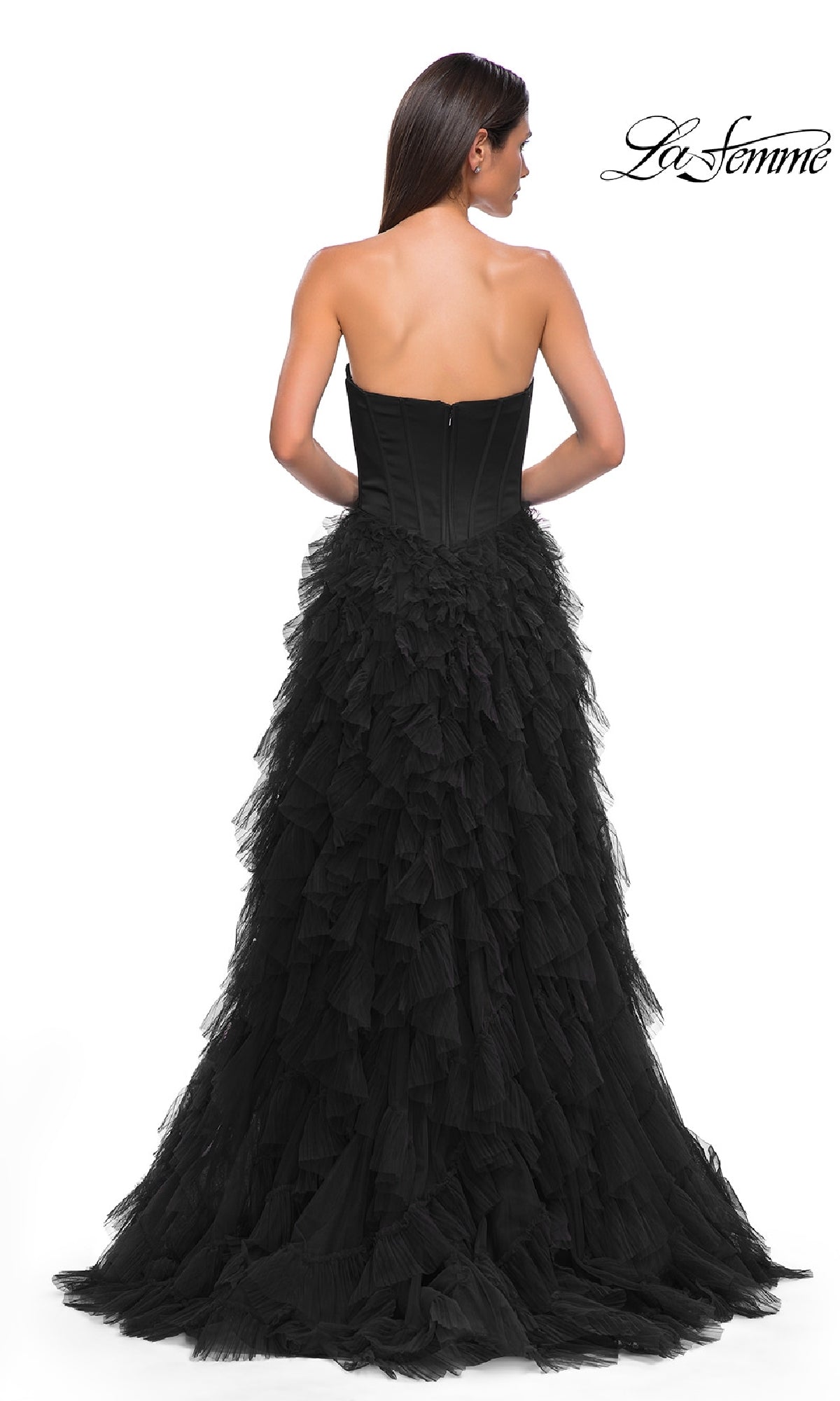 A woman in the Strapless Long Ruffled Prom Dress: La Femme 32760, featuring a black, corset-style bodice and ruffled skirt, stands with her back to the camera against a white background. The La Femme logo is in the top right corner.